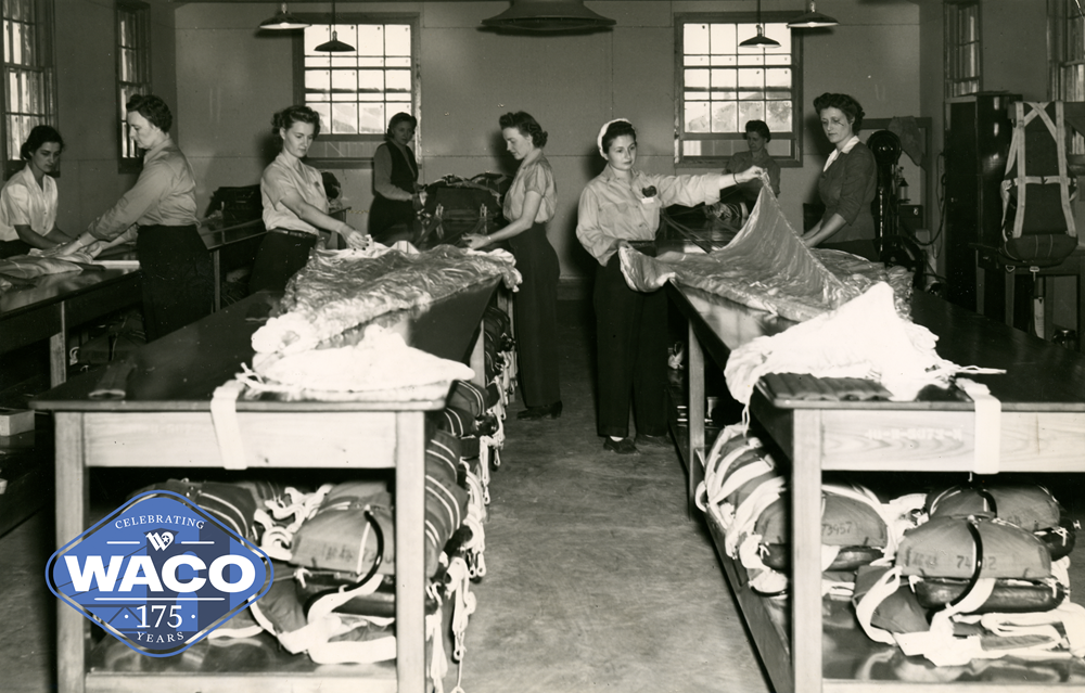 Black and white photo of women packing parachutes on long tables