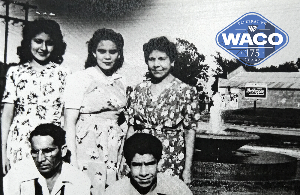 Black and white photo of three Hispanic women and two Hispanic men in front of La Pila water fountain