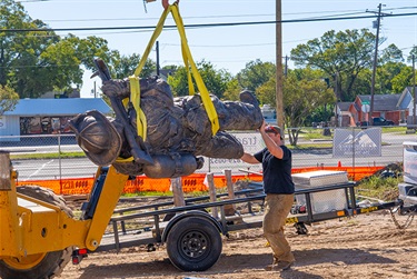 Construction workers lifting the statue off the trailer with machinery.