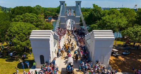 Aerial photo of Waco Suspension Bridge with onlookers watching a longhorn cattle drive across it to commemorate the grand reopening of the bridge.