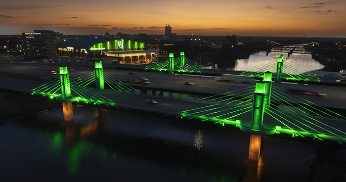Aerial photo of the I35 bridge lit up in Green with Foster Pavilion and Alico buildings behind it.