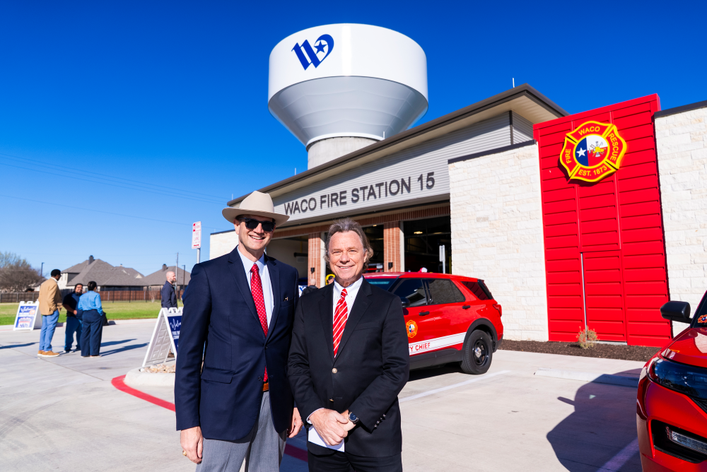 Two men standing in front of Fire Station 15. Water tower peaking behind.