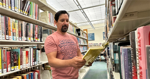 A man reading a book in a library aisle
