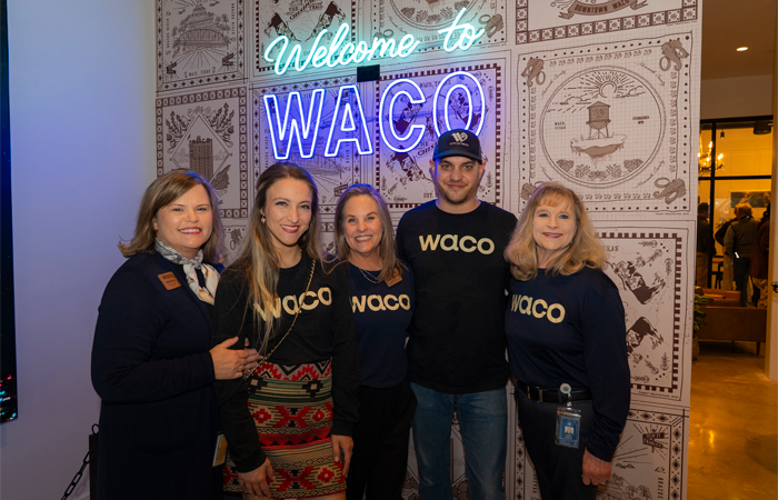 Five Welcome Center staff standing at Welcome to Waco neon sign