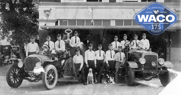 Black and white photo of fire men, a dog, and two fire engines