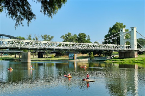 A group of people paddle board on the river near the Waco Suspension Bridge.