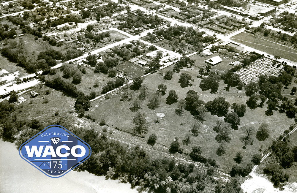 Black and white photo of an aerial view of a cemetery and a surrounding neighborhood